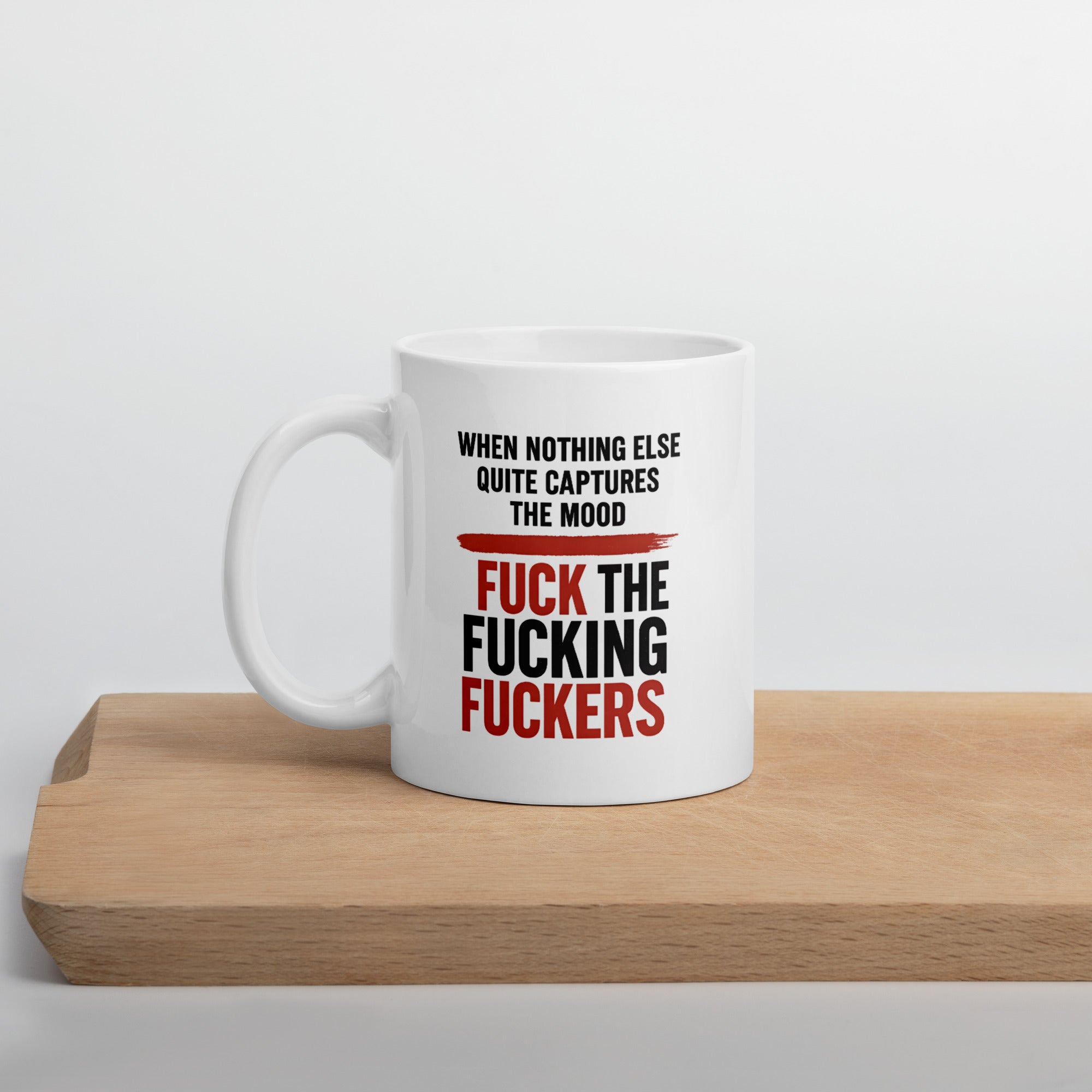 White mug with bold black and red text that says, “When nothing else quite captures the mood, fuck the fucking fuckers.”