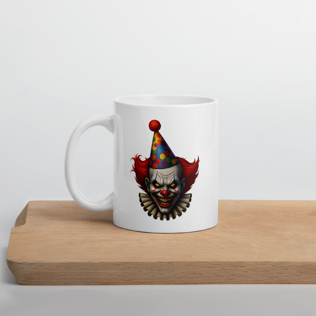 White mug with a creepy clown illustration featuring red hair, a sinister grin, and a colorful polka dot party hat.