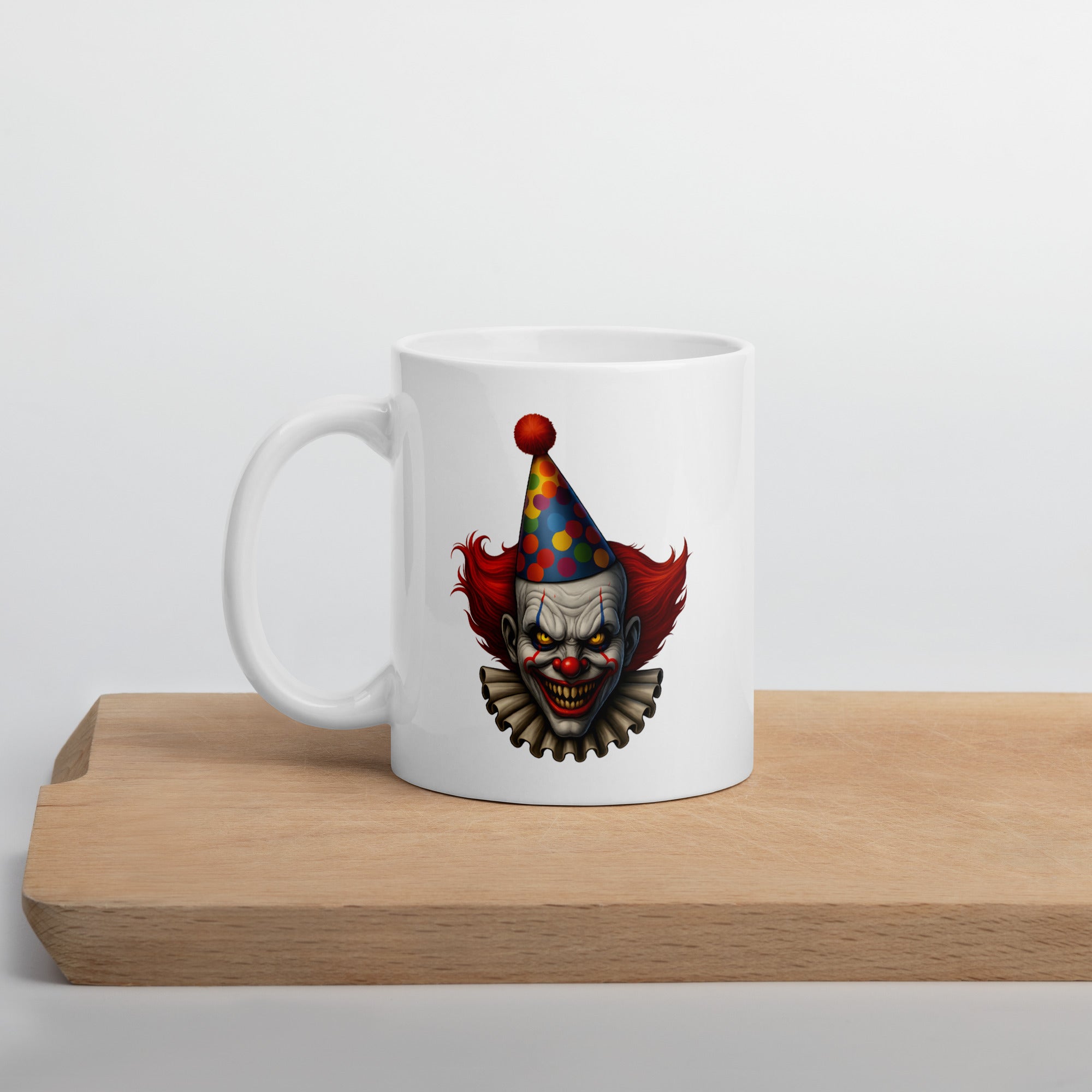 White mug with a creepy clown illustration featuring red hair, a sinister grin, and a colorful polka dot party hat.