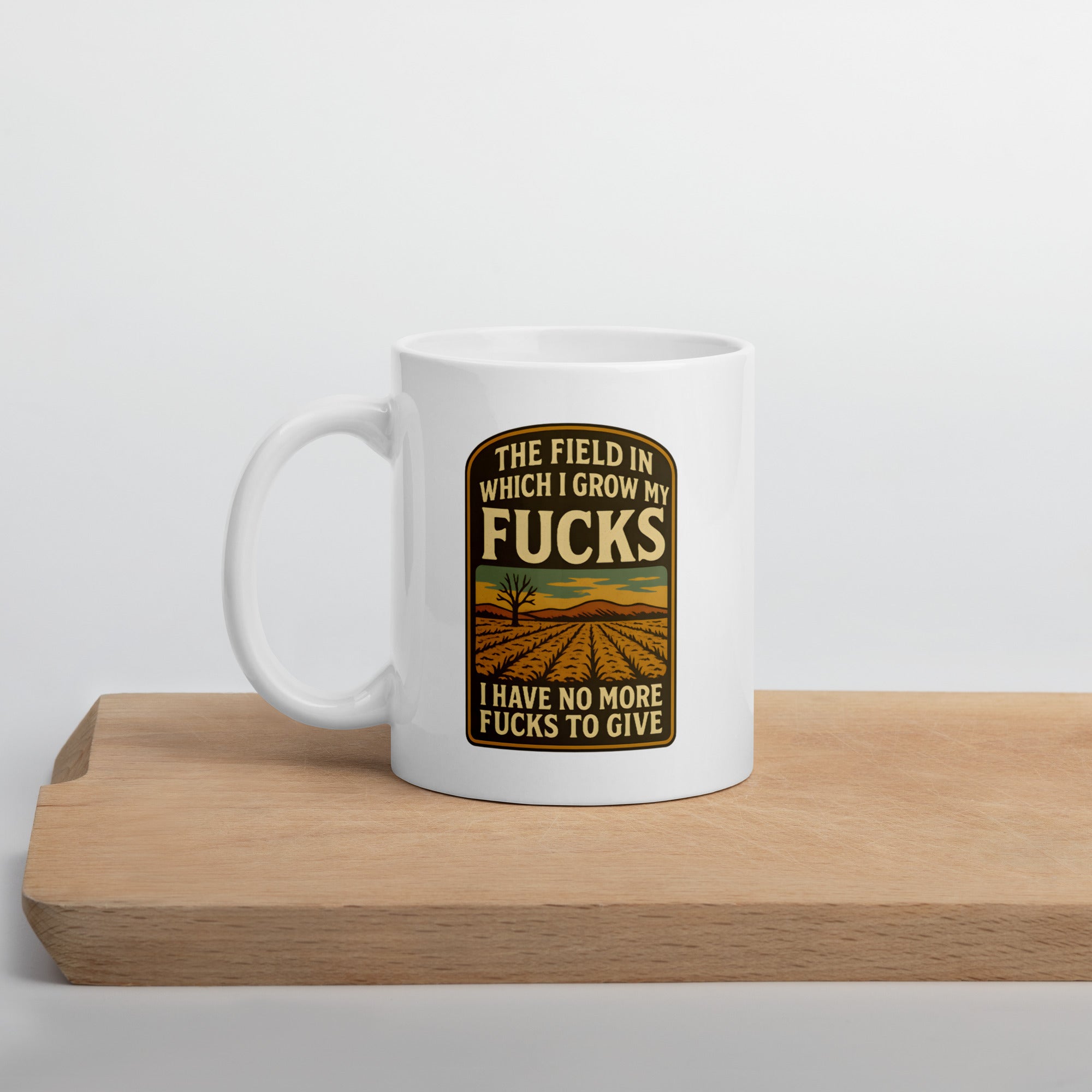 White mug with a framed design of a barren field and text that says, “The field in which I grow my fucks. I have no more fucks to give.”