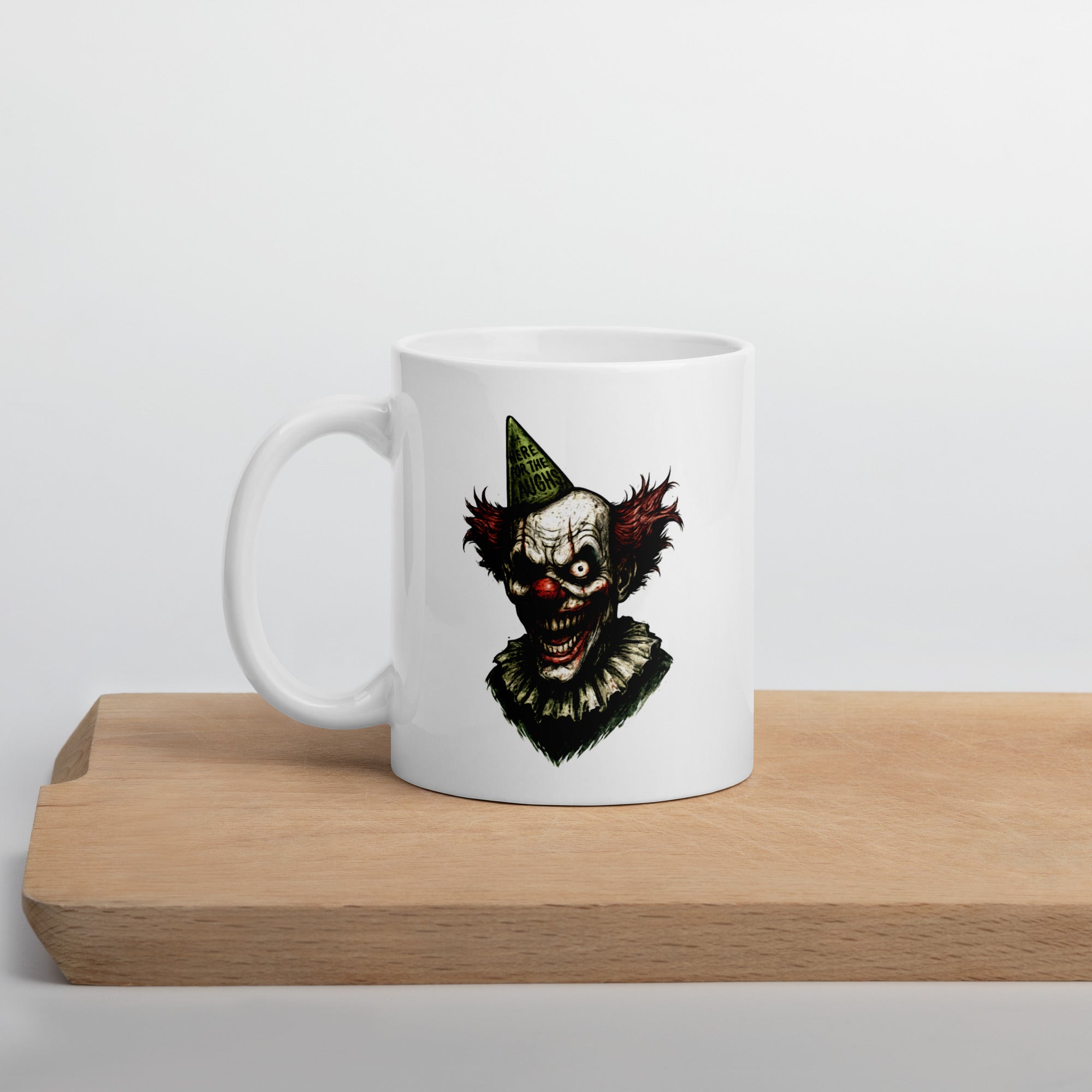 White mug with a creepy clown illustration, featuring a sinister grin, red hair, and a green party hat.