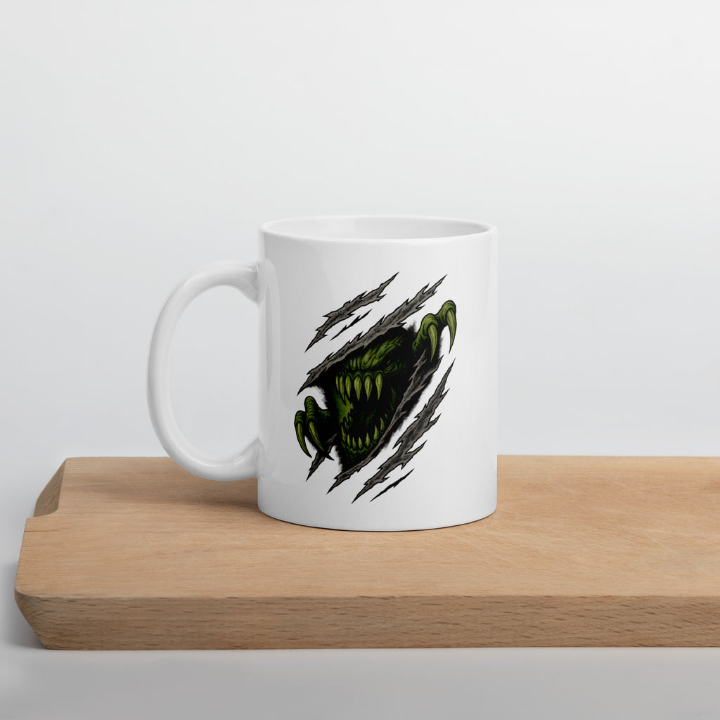 White mug with a graphic of a green monster face and claws tearing through the surface, surrounded by claw marks.