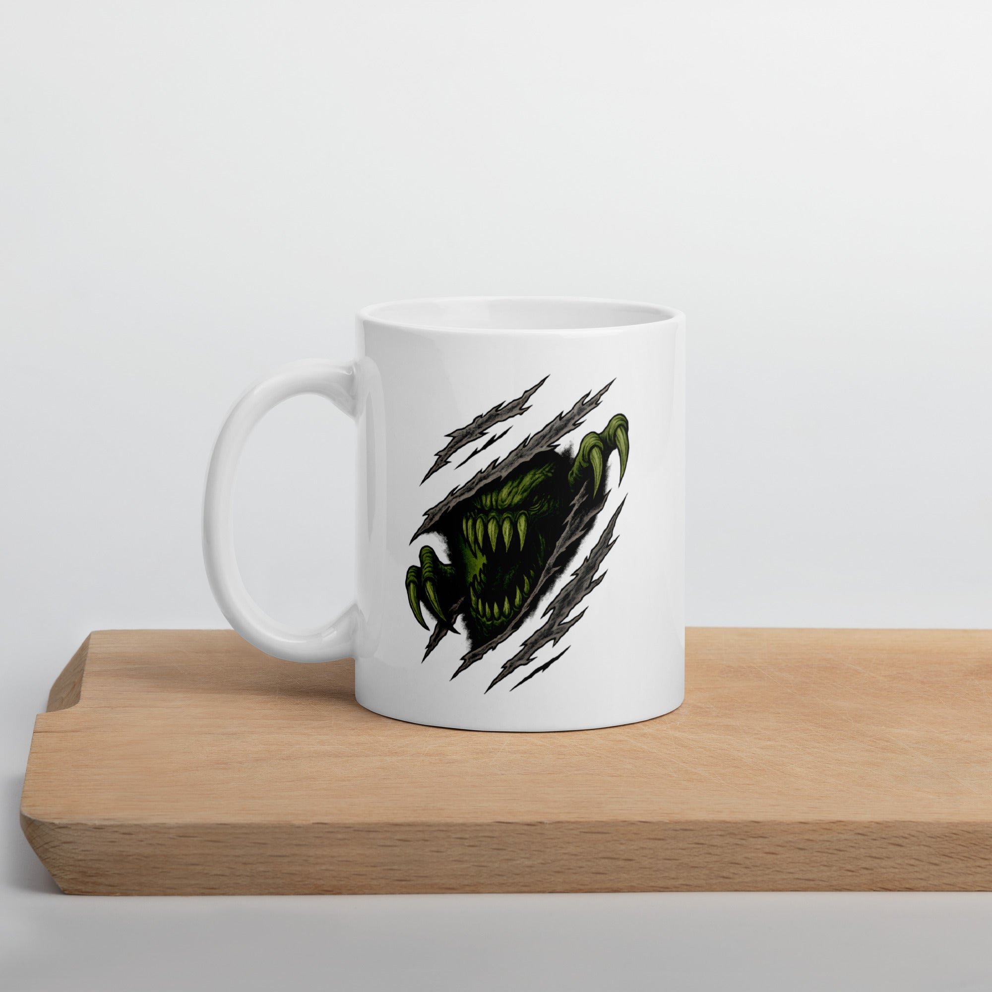 White mug with a graphic of a green monster face and claws tearing through the surface, surrounded by claw marks.